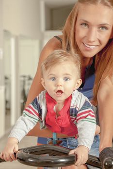 Young beautiful mother and her cute little baby boy having fun in a cycling gym.