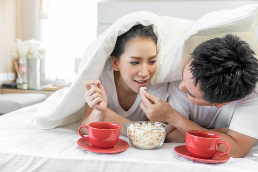 Young Asian Couples having breakfast on bed together in bedroom of contemporary house for modern lifestyle concept