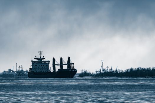 Blue bulk carrier sailing to the sea in cold winter. Monochrome