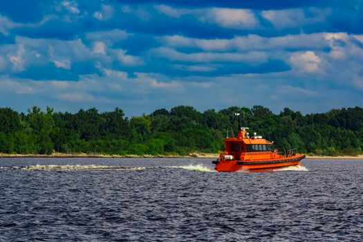 Orange pilot boat moving by the river in Europe. Rescue service