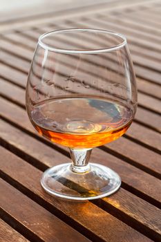 Glass of cognac standing on a wooden table in sunlight.
