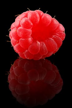 One ripe raspberry on black background.