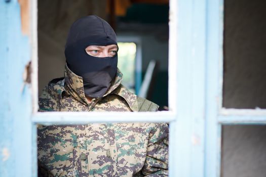 Military camouflage with a rifle on a background of bombed buildings.