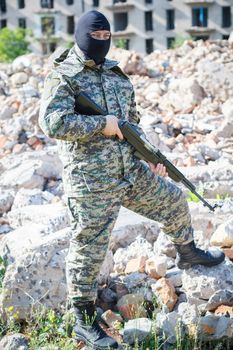 Military camouflage with a rifle on a background of bombed buildings.