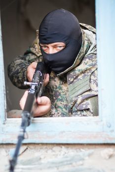 Military camouflage with a rifle on a background of bombed buildings.