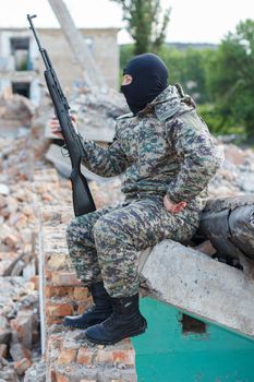 Military camouflage with a rifle on a background of bombed buildings.