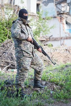 Military camouflage with a rifle on a background of bombed buildings.