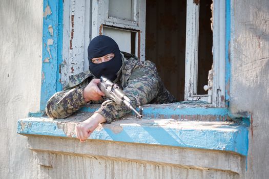 Military camouflage with a rifle on a background of bombed buildings.