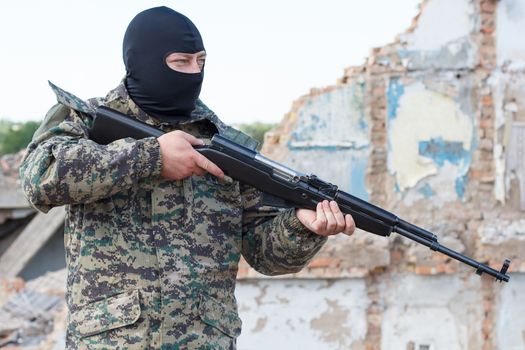 Military camouflage with a rifle on a background of bombed buildings.