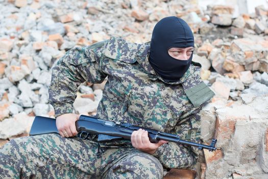 Military camouflage with a rifle on a background of bombed buildings.