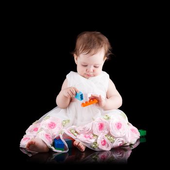 The girl is one year in dress sitting on a black background.