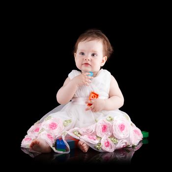 The girl is one year in dress sitting on a black background.