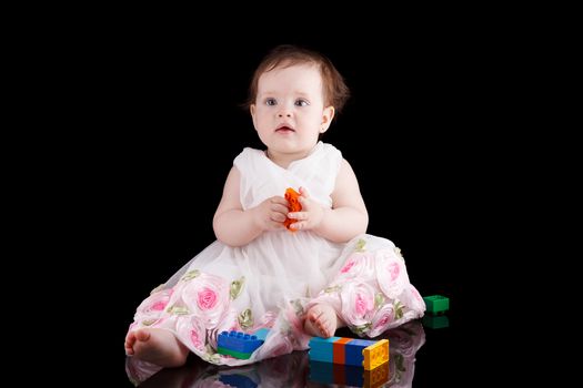 The girl is one year in dress sitting on a black background.