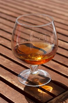 Glass of cognac standing on a wooden table in sunlight.