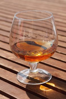 Glass of cognac standing on a wooden table in sunlight.