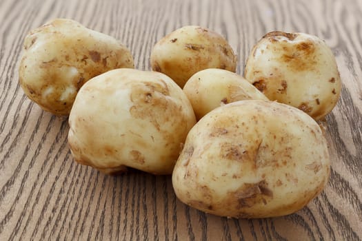 Heap of raw potato lying on the wooden background.