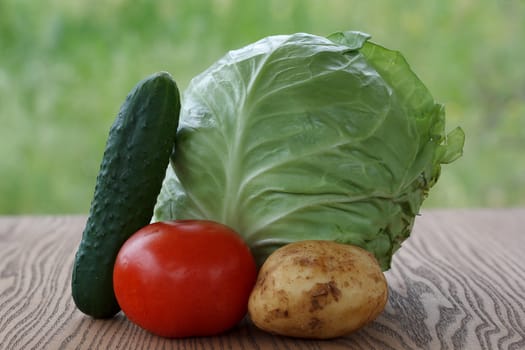 One juicy cabbage, tomato, cucumber and potatoes on wooden background.
