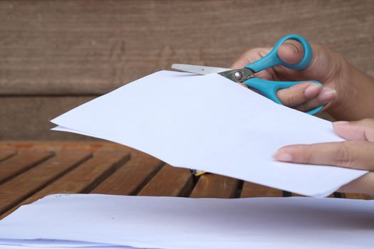 Hand cutting paper with scissors at the table.