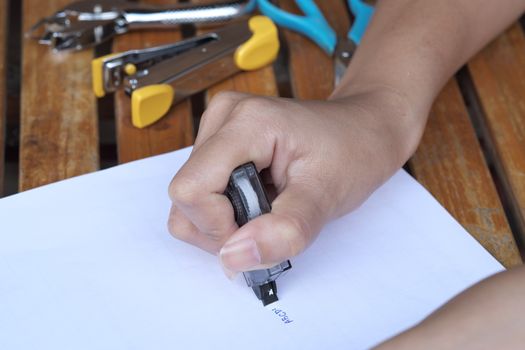 Hand holding black correction tape roller on table.