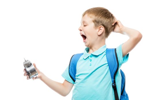 tired yawning schoolboy with an alarm clock on white background