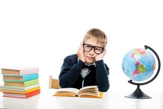 portrait of a dreamy schoolboy at a table with books and a globe isolated