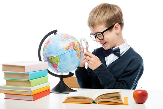cheerful schoolboy with a magnifying glass examines the globe at the table, portrait is isolated