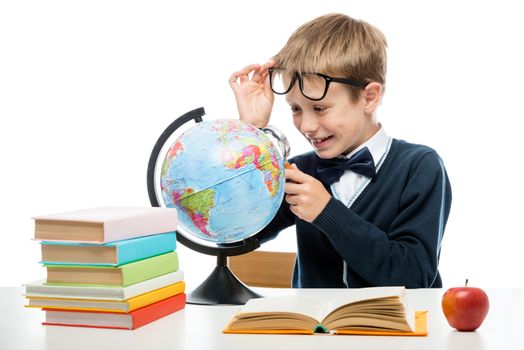 portrait of a happy schoolboy with a magnifying glass studying a globe against a white background