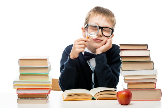 boy with magnifier at the table with a pile of books on a white background
