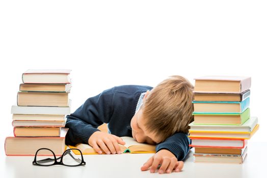 tired schoolchild is sleeping at a table between piles of books on a white background