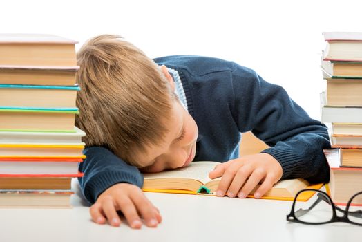 schoolboy is sleeping at a table between piles of books on a white background