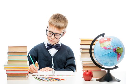 very smart schoolboy with glasses with books at the table on a white background
