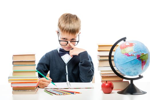 boy in glasses and uniform doing lessons at the table, portrait in studio isolated