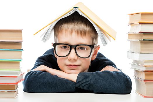 close-up portrait of a smart schoolboy wearing glasses with a book on his head