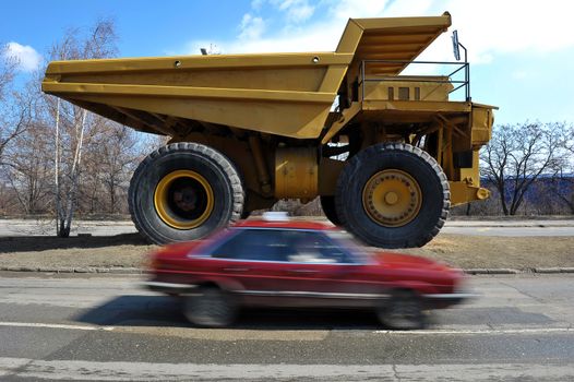 Small cars passing by big yellow mining truck