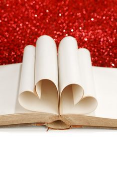 Pages of open book rolled in heart shape on glitter background