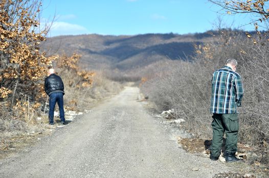 Two men urinating on the side of the road
