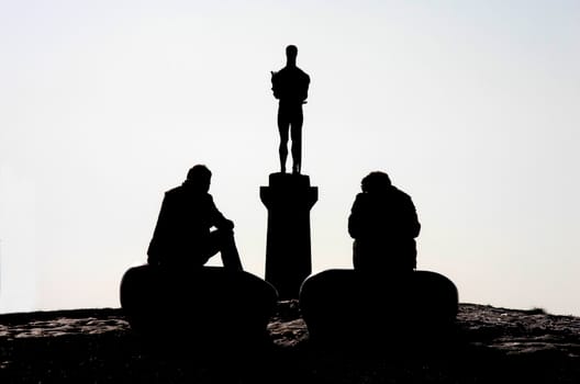 Two men sitting in front of statue of Pobednik in Belgrade at sunset