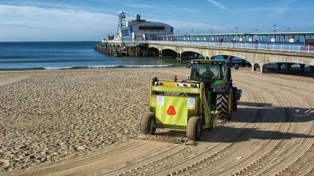 A tractor cleans the sand by raking it and picking up debri on the beach  at the english seaside town of Bournemouth