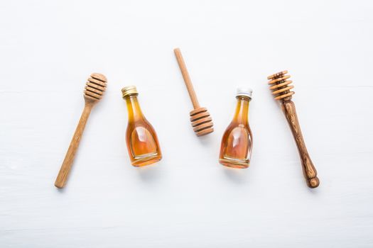 Honey wooden dipper and little honey bottle on white wooden background.