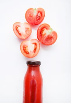 Tomatoes juice in bottle and fresh tomatoes slices on white wooden background.