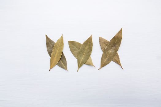 Dried bay leaves on white wooden background.
