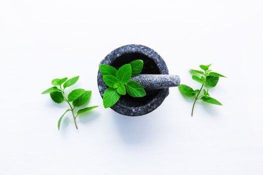 Stone mortar and pestle with peppermint leaf on white wooden background with copy space.