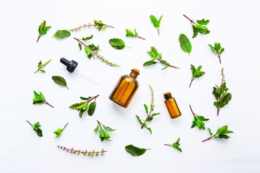 Holy Basil Essential Oil in a Glass Bottle with Fresh Holy Basil white wooden background.