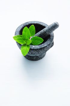 Stone mortar and pestle with peppermint leaf on white wooden background with copy space.