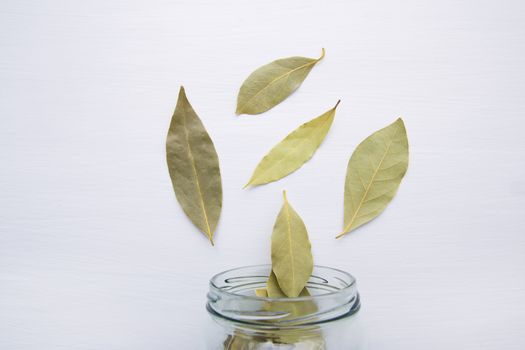 Dried bay leaves in glass jar on white wooden background.