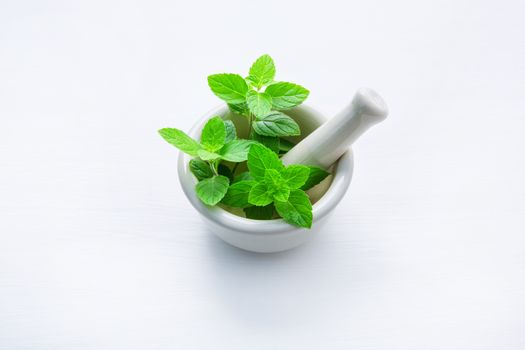 White porcelain mortar and pestle with peppermint leaf on white wooden background with copy space.