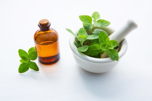 Natural Mint Essential Oil in a Glass Bottle with Fresh Mint Leaves in white porcelain mortar.