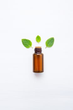 Natural Mint Essential Oil in a Glass Bottle with Fresh Mint Leaves on white wooden background.