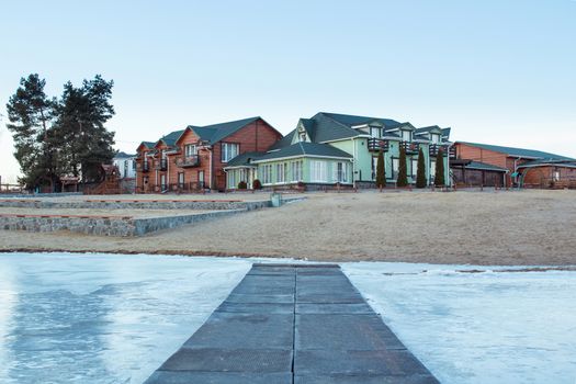 Winter village house on sandy beach near cold frozen river lake