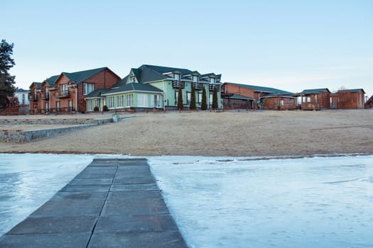 Winter village house on sandy beach near cold frozen river lake